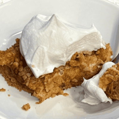 Gluten-free dairy-free pumpkin dessert with golden crumble topping and whipped coconut cream on white plate