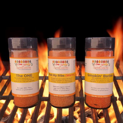 Grilling Bundle of spice blends for grilling or smoking including The ONE, Rub My Ribs (Warm), and Smokin' Barbie in jars on a flaming grill
