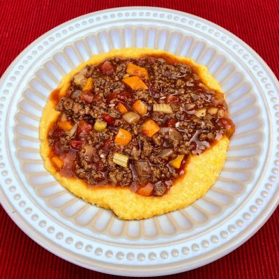 Beef and Veggie Sauce over Cheesy Grits seasoned with The ONE in a white bowl on a red placemat
