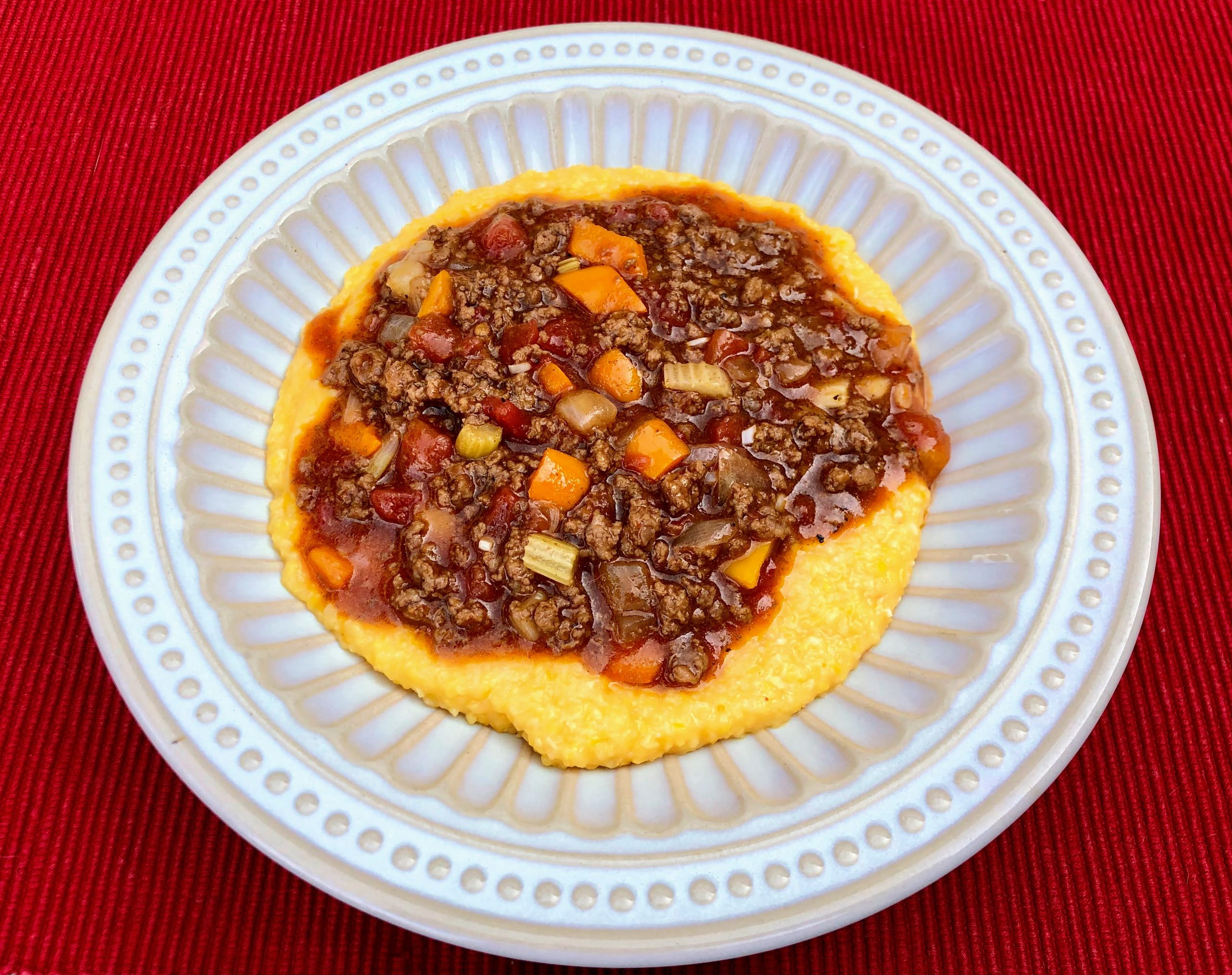 The ONE Beef and Veggies with Cheesy Grits in a white bowl on a red placemat