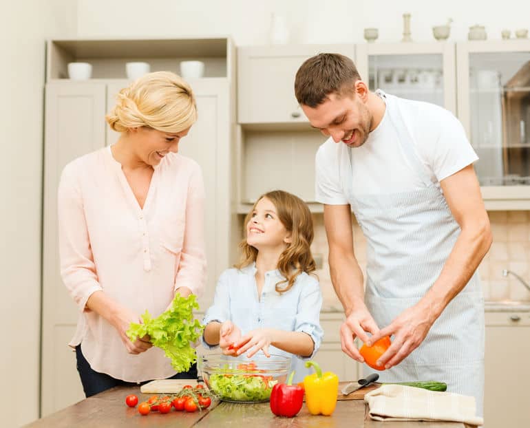 happy family making dinner in kitchen Mother, father, and young daughter preparing a salad together in a kitchen