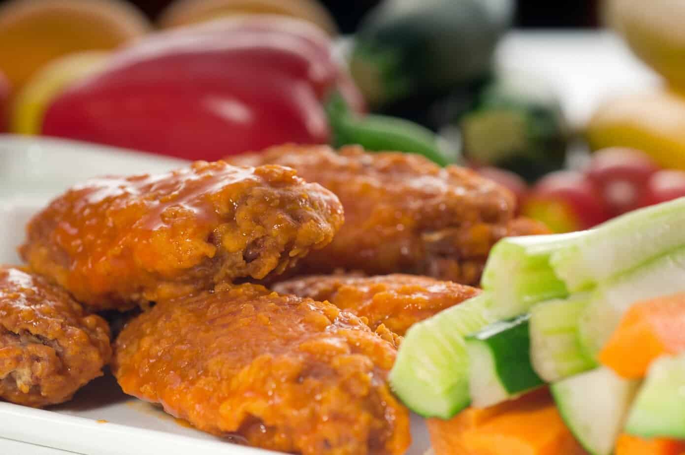 Crispy buffalo chicken wings coated in orange sauce, served with fresh cucumber and carrot sticks