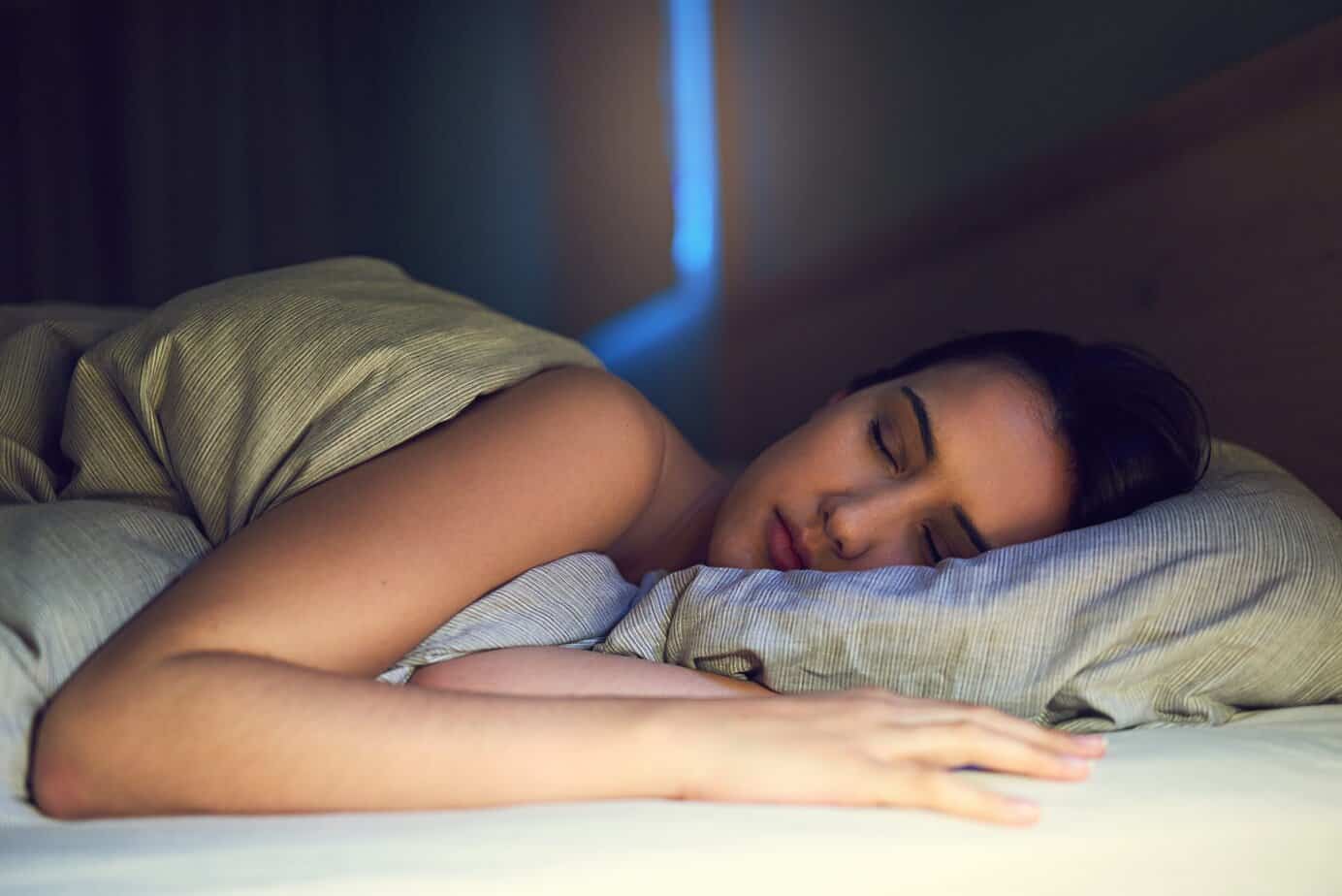 Getting a good nights sleep. Shot of a young woman sound asleep in her bedroom Young woman asleep on her side in a dimly lit bedroom, resting comfortably on a pillow with a blanket pulled up around her shoulders