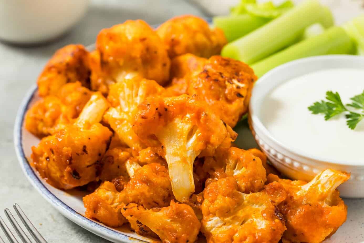 Plate of roasted buffalo cauliflower wings with celery sticks and ranch-style dipping sauce