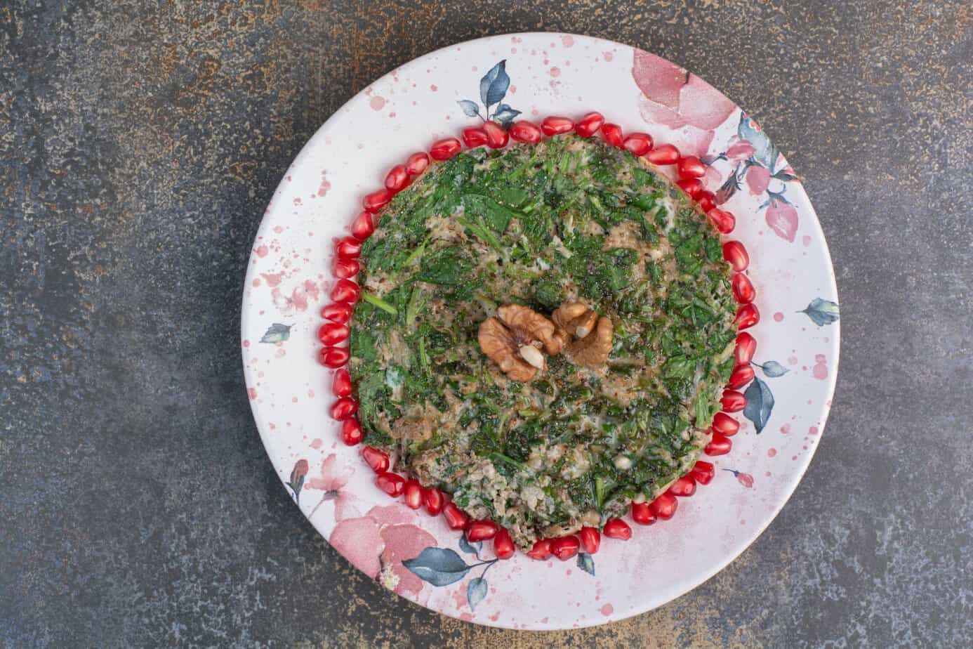 Herbed scrambled eggs garnished with fresh pomegranate seeds, served on a floral plate, showing a savory, Persian-inspired breakfast option