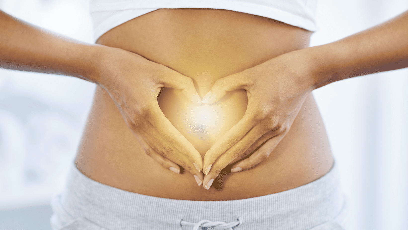 Hands forming a heart shape over the abdomen with a warm healing glow at the center representing gut health and intestinal healing