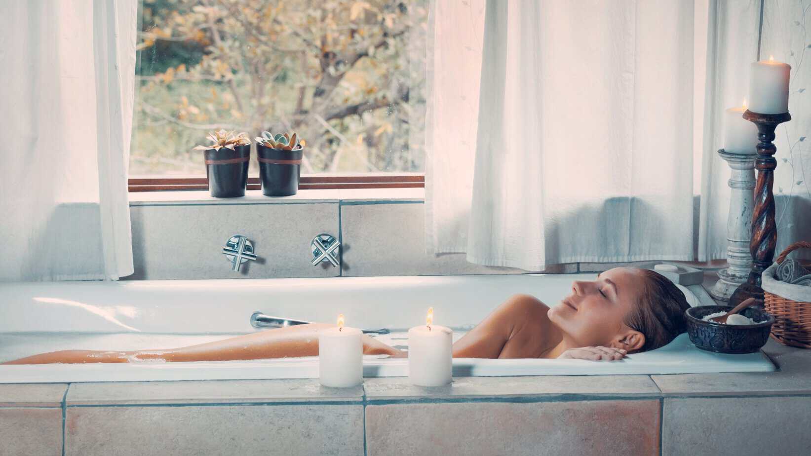 Happy woman at spa resort A woman resting with eyes closed in a warm bath, with two white candles on the edge of the tub