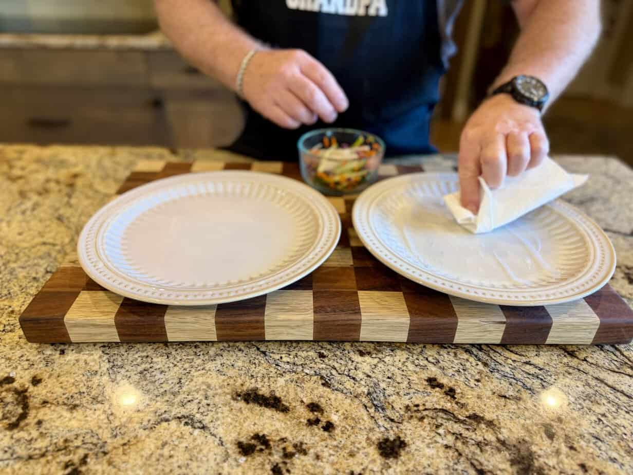 Blotting spring roll wrapper after dipping Hands gently blotting a softened rice paper wrapper with a paper towel to remove excess moisture before filling rainbow salad rolls