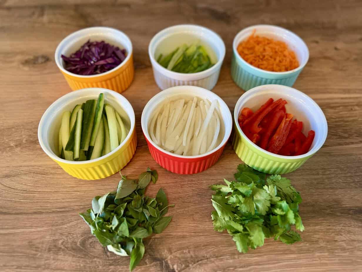 Salad Roll Ingredients w-o wrappers Fresh vegetables and herbs in colorful ramekins for rainbow salad rolls including purple cabbage, carrots, red pepper, cucumber, daikon, and scallions